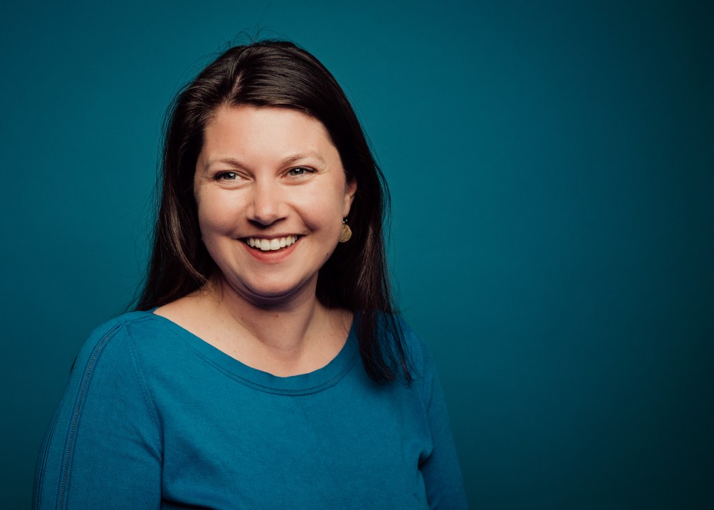 Photograph of Corey Barber smiling in front of a teal background.