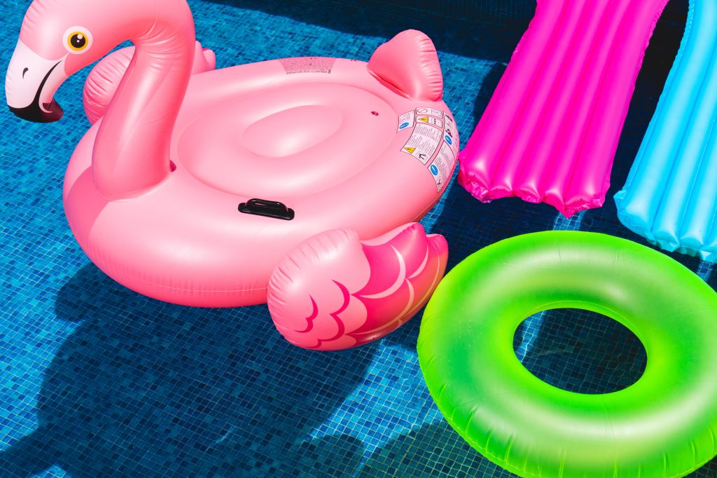 A flamingo floaty next to several normal floatys in a sunny pool
