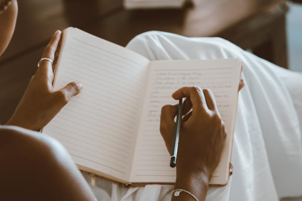 Over the shoulder view of a brown skinned person writing in a journal.