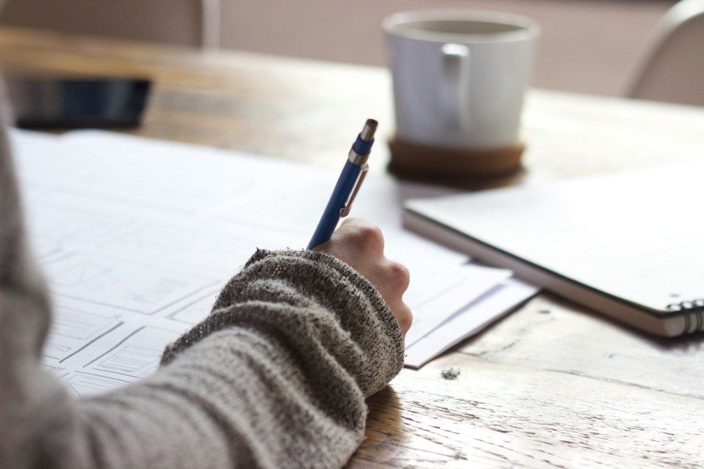 Someone writing at a desk with natural light and a cup of coffee.